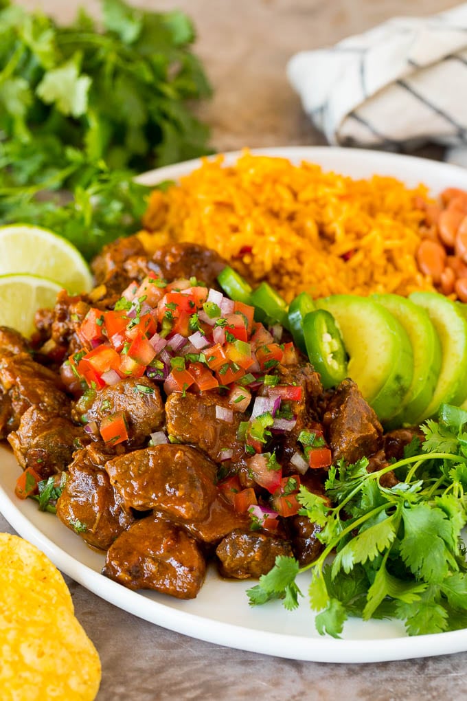 This Mexican style carne guisada is beef that is stewed with tomatoes, peppers and spices until it becomes tender and flavorful. Carne guisada served with rice, beans and avocado.