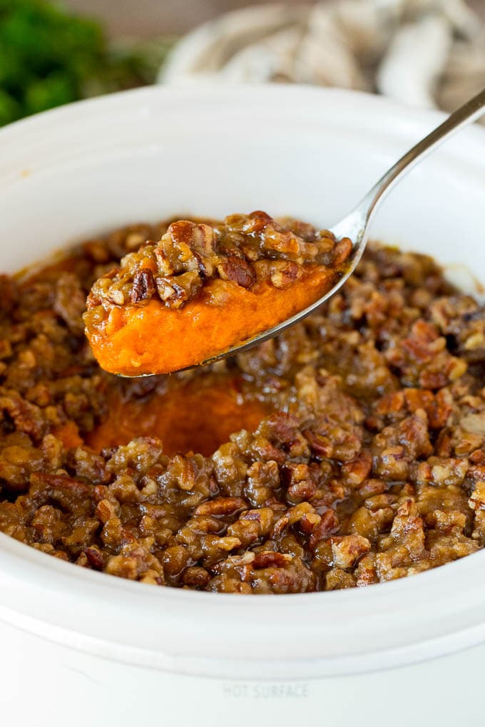This crock pot sweet potato casserole is yams mashed with sweetener, vanilla and spices, then finished off with a brown sugar pecan topping. A spoon serving up a portion of crock pot sweet potato casserole.