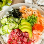 A sushi bowl topped with salmon, ahi, avocado, cucumber and nori.