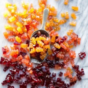 A picture of a metal scoop holding red, orange and yellow gummy bears.