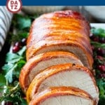A plate of bacon wrapped pork loin which is pork loin roast brushed with a sweet and savory glaze, then covered in bacon.