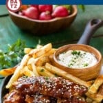 A pan of baked sesame chicken fingers which are tossed in a sweet and tangy Asian-style honey, soy and sesame sauce and are served with fries and a creamy sesame dip.