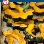 A sheet pan of roasted acorn squash slices garnished with parsley.
