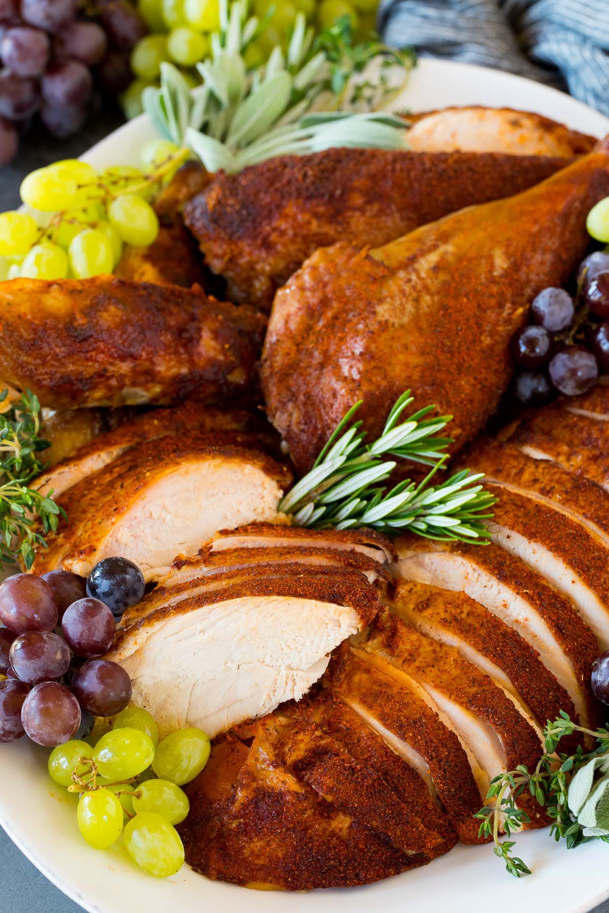 Sliced smoked turkey garnished with grapes and herbs on a platter.