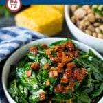A bowl of collard greens with bacon on top with a side of cornbread and hoppin' johns.