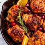A skillet of cranberry chicken thighs with fresh cranberries, orange and rosemary.