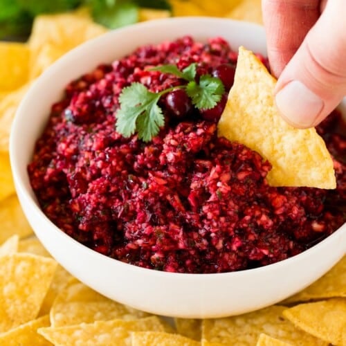 A hand scooping up some cranberry salsa with a tortilla chip.