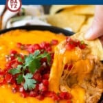 A skillet of creamy bean dip being scooped by a tortilla chip.