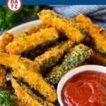 A plate of fried zucchini on a plate with a small bowl of marinara sauce.