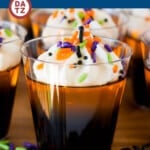 These Halloween Jello shots are layers of black cherry Jello and orange Jello, mixed with vodka and served with a topping of whipped cream and sprinkles.