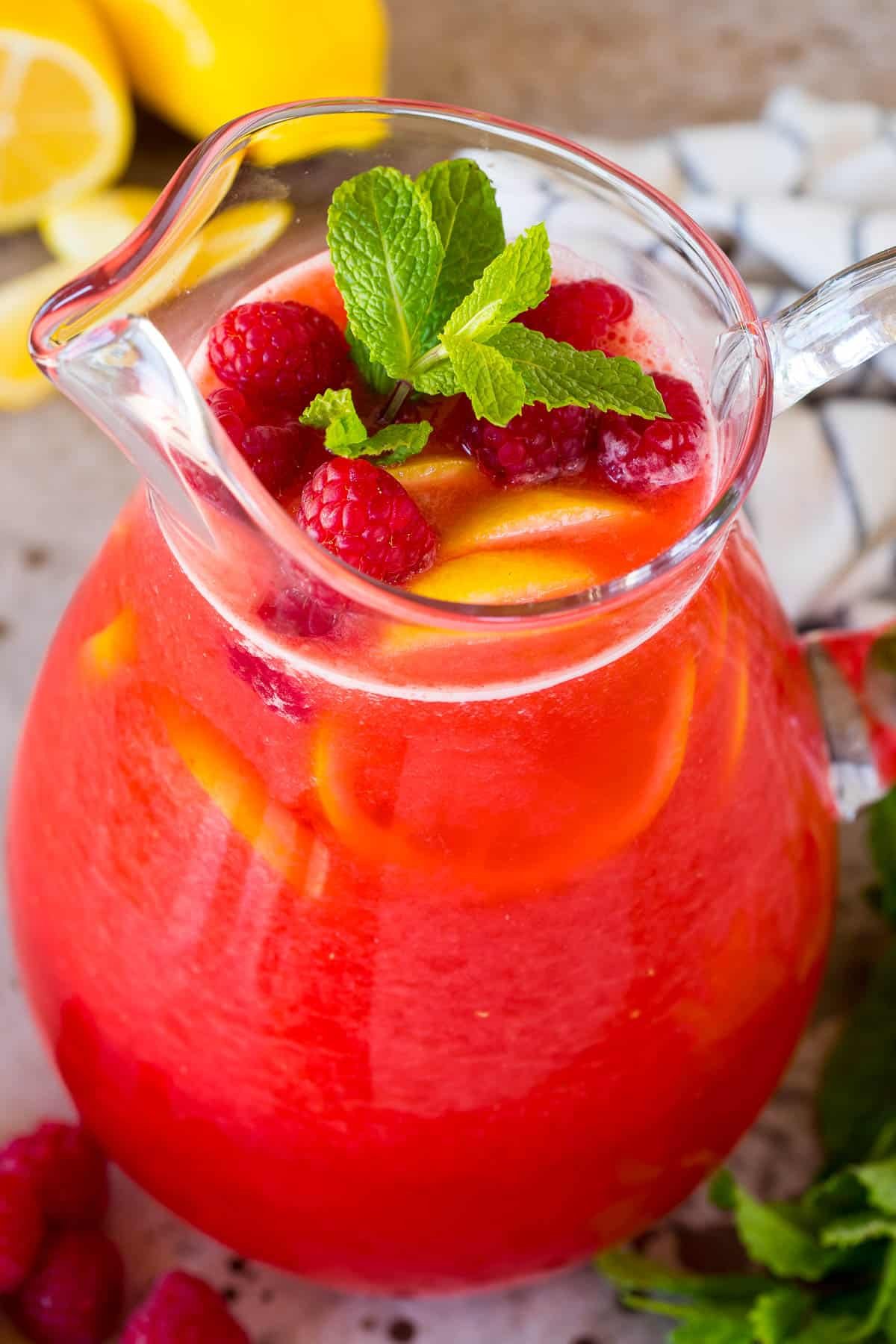 A pitcher of raspberry lemonade with mint and lemon slices in it.