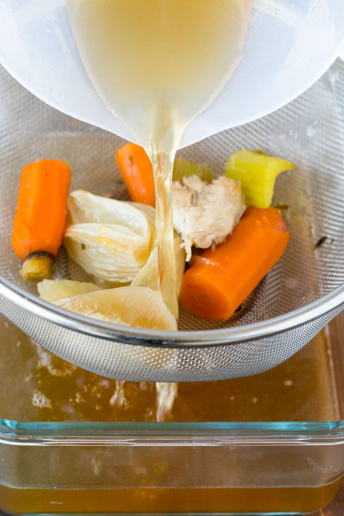 Broth being poured through a mesh strainer.
