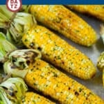A tray of grilled corn on the cob with butter sauce and parsley.