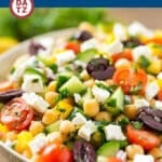 A bowl with a chopped Greek salad featuring fresh vegetables and a tangy Greek dressing.