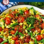 A pan with succotash including corn, green beans, lima beans, cherry tomatoes and bacon.