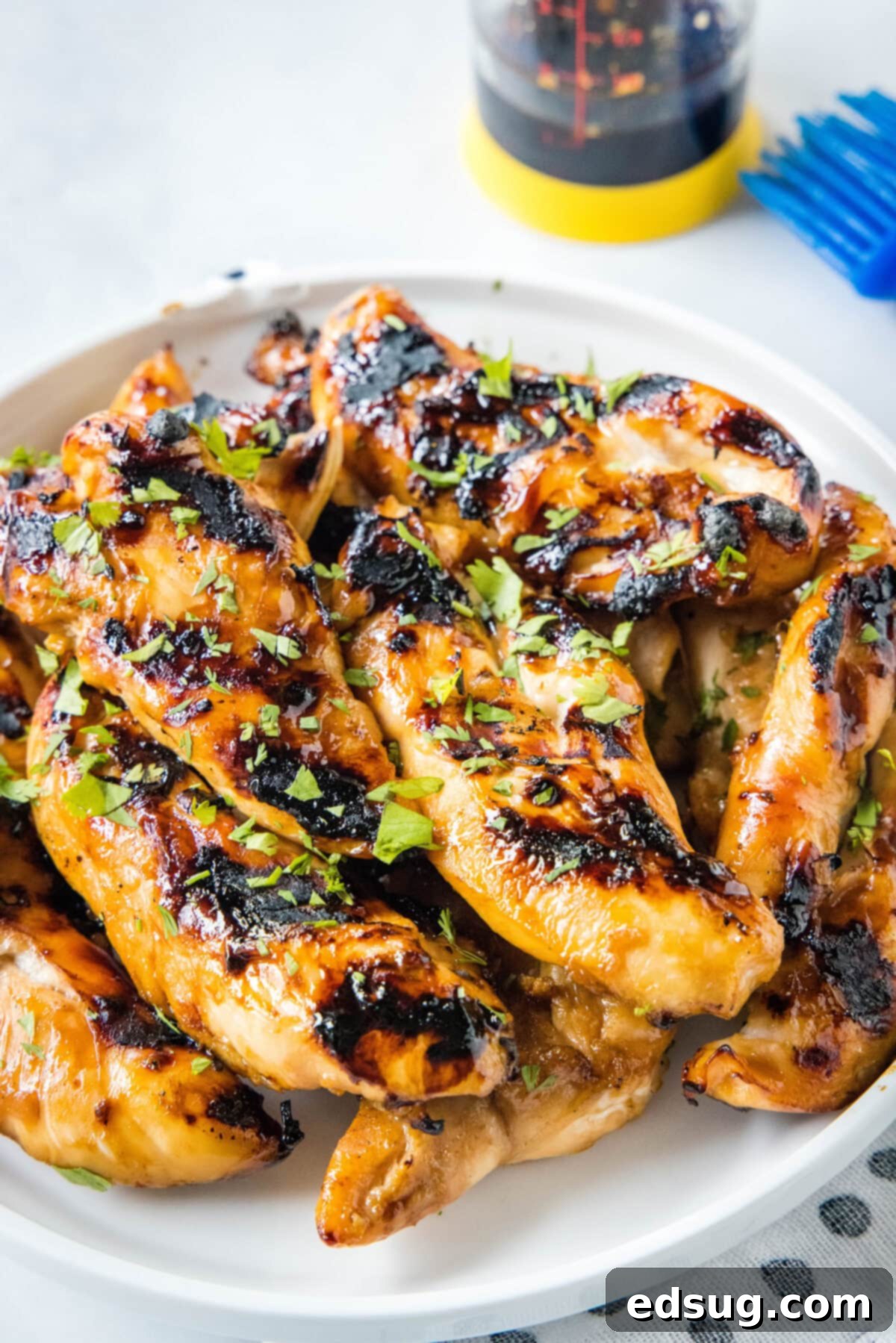 Teriyaki grilled chicken piled on a white platter, garnished with sesame seeds and green onions.