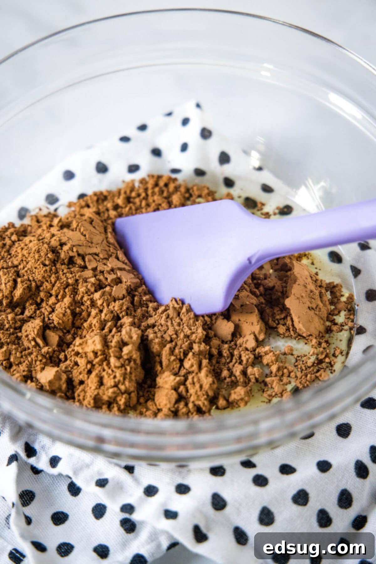 A mixing bowl with cocoa powder and a rubber spatula, showing the initial mixing step.