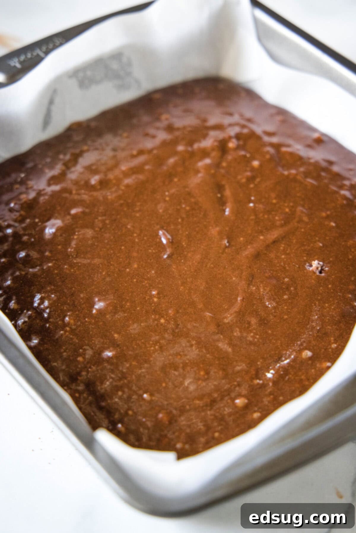 A square baking dish filled with smooth brownie batter, ready for the oven.