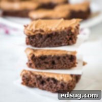 Three brownie squares with frosting stacked on top of each other.
