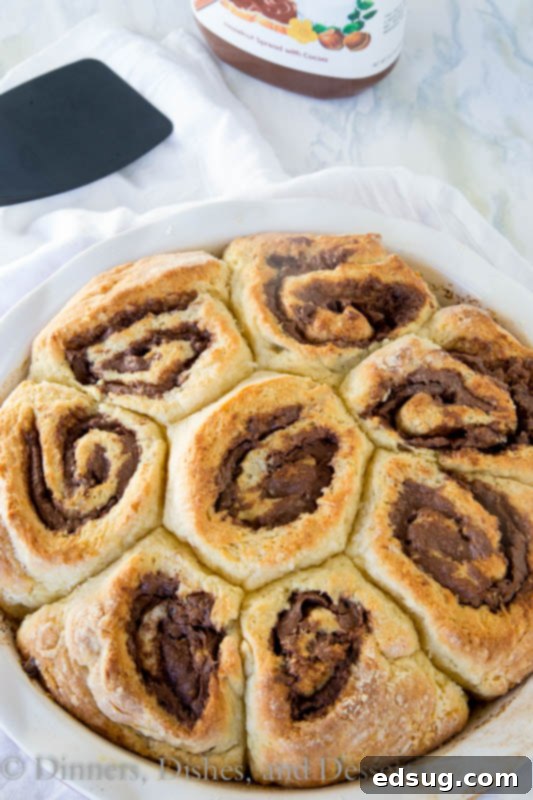 Nutella cinnamon rolls baking in a round pan, golden brown and bubbly.