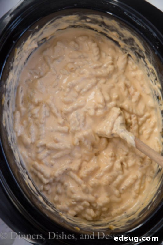 Ultimate Crock Pot Mac and Cheese 3 Uncooked pasta, milk, and cheeses being mixed in a slow cooker