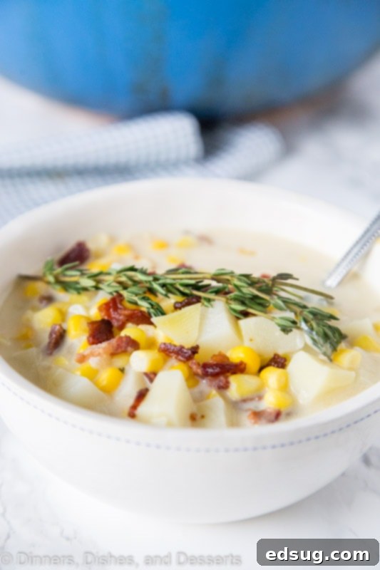 A close-up of potato corn chowder in a rustic bowl, garnished with bacon and fresh thyme.