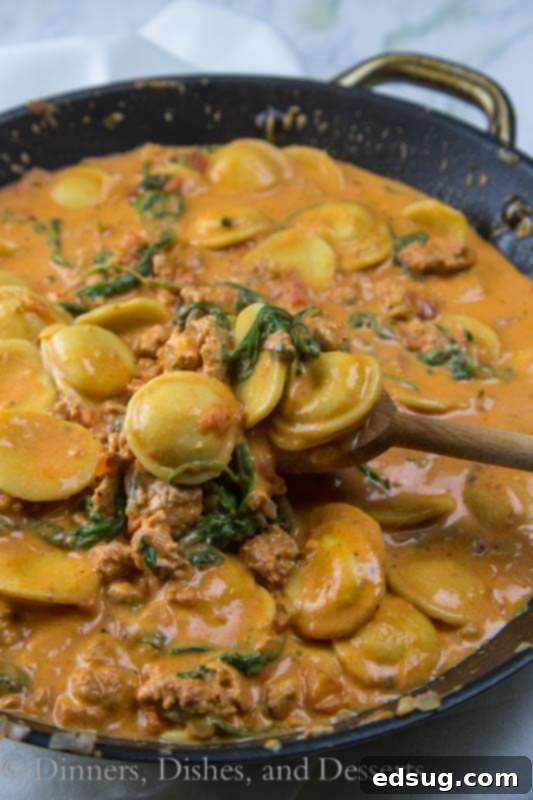 Close-up of creamy sausage and tomato ravioli, highlighting the texture of the sauce, plump ravioli, and bits of sausage and spinach.