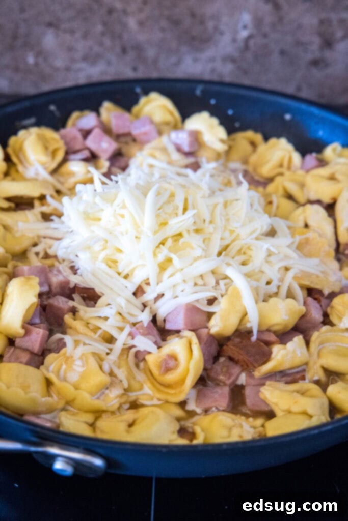 Shredded cheese added to a skillet with ham tortellini.