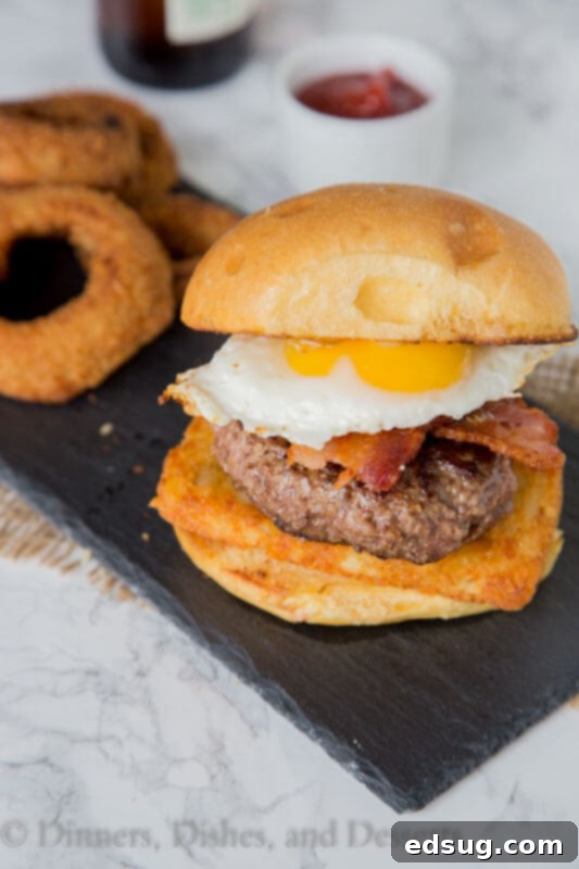 A stack of breakfast burger components: hash brown, patty, cheese, bacon, and a fried egg.
