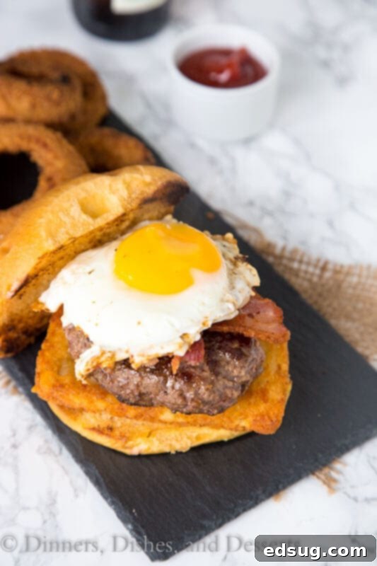 The finished breakfast burger, messy and delicious, with a side of onion rings.