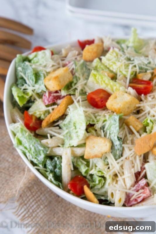 A large bowl of creamy Caesar pasta salad with fresh romaine lettuce, cherry tomatoes, and parmesan cheese, ready to be served at a summer gathering.