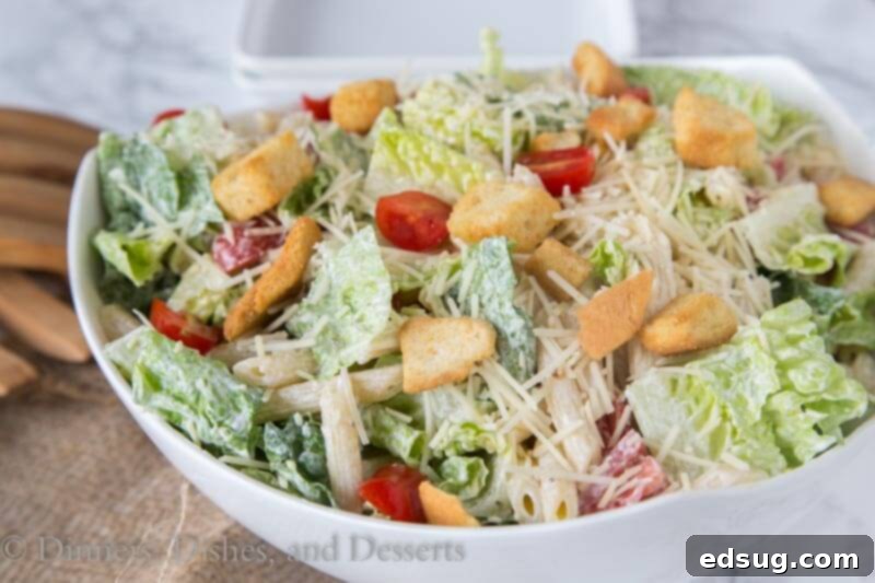 Close-up of Caesar pasta salad in a bowl, showcasing the creamy dressing coating the pasta, lettuce, and tomatoes, with visible parmesan and croutons.