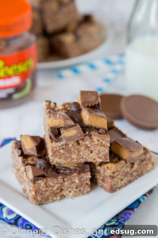 A stack of Reese's Peanut Butter Rice Krispie Treats drizzled with chocolate and topped with mini peanut butter cups.