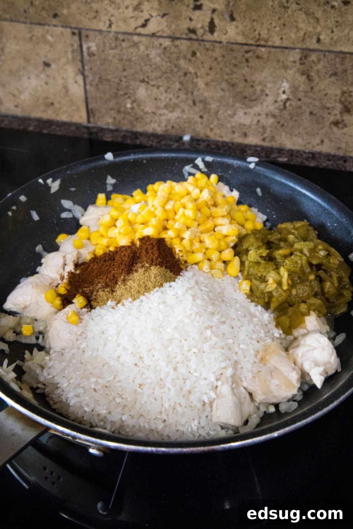 adding rice, corn, green chiles and spices to skillet with cooking chicken