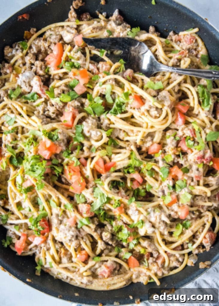 Taco-flavored spaghetti with ground beef and cheese in a large skillet, ready to serve.