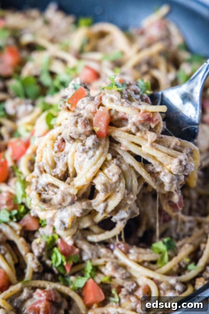 A spoonful of creamy taco spaghetti being lifted from a skillet, showing the cheesy sauce and meat.