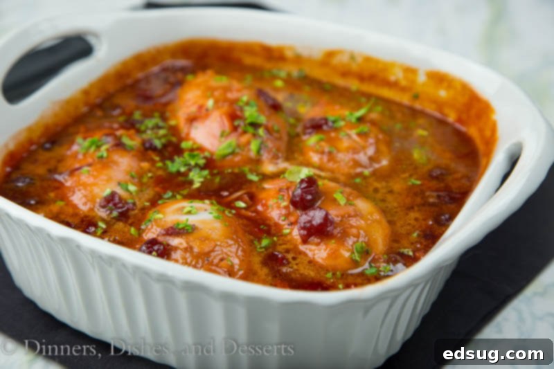 Close-up of golden-brown Cranberry Chicken baking in a glass pan, coated in a thick, vibrant sauce