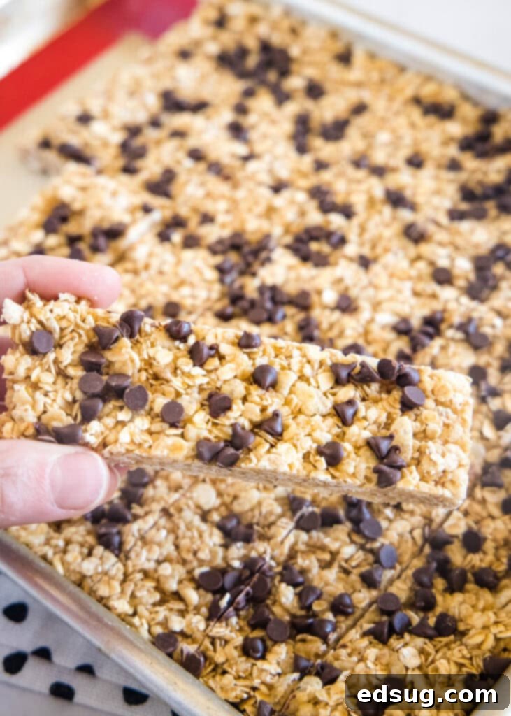 A hand holding a homemade chewy granola bar over a baking pan, showcasing its perfect texture.