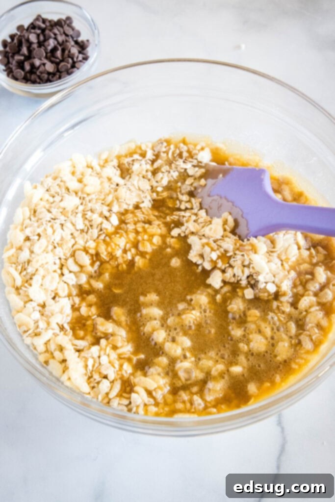Pouring the warm honey and butter mixture into a bowl of oats and crispy rice cereal.
