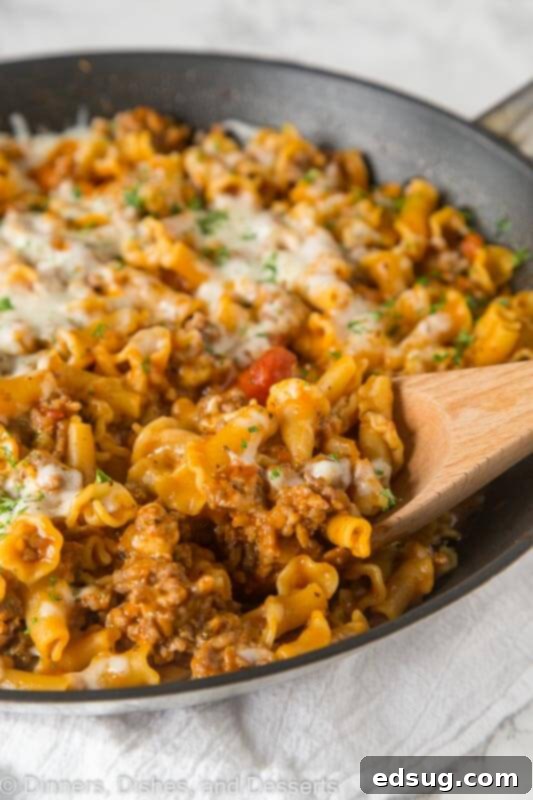 A close-up of a large skillet brimming with steaming Homemade Hamburger Helper Lasagna, topped with melted cheese and fresh basil.