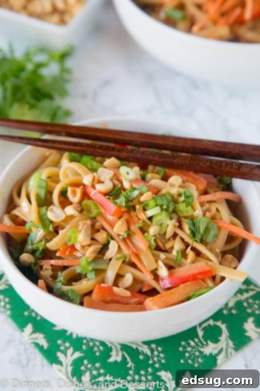 A close-up of Thai Peanut Noodles in a white bowl with chopsticks, showing the texture and ingredients.
