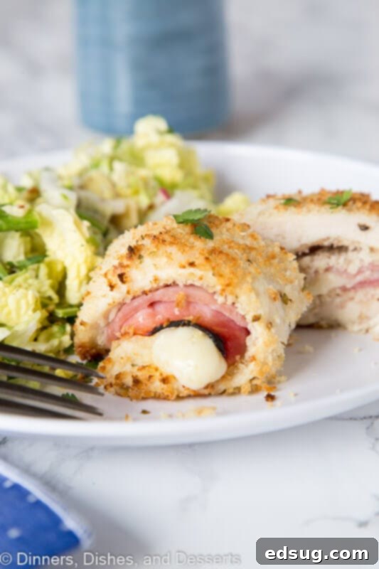 A beautifully plated Crispy Chicken Cordon Bleu, sliced open to reveal the melty Swiss cheese and ham filling, garnished with fresh parsley.