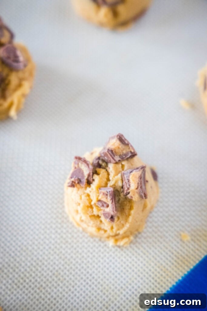 Cookie dough balls on a baking sheet, with chopped Reese's Peanut Butter Cups pressed into the tops, ready for baking.