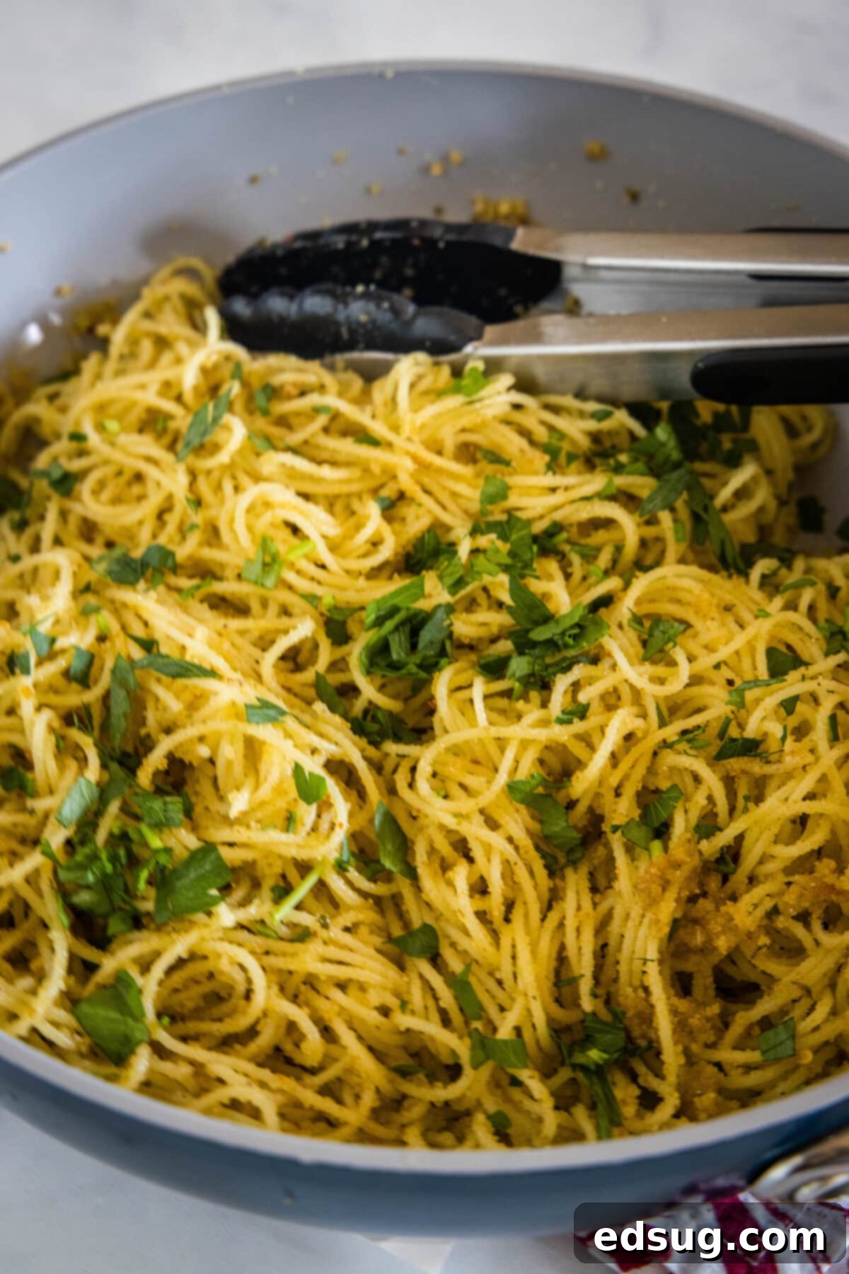 Golden Garlicky Crumb Pasta 4 Looking down into a skillet where cooked spaghetti is being tossed with golden breadcrumbs and fresh herbs.