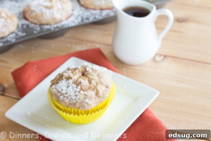 three French toast muffins on a plate, dusted with powdered sugar and drizzled with syrup