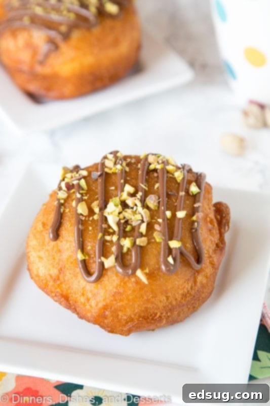 multiple Nutella donuts on a serving plate, drizzled with more Nutella and topped with pistachios