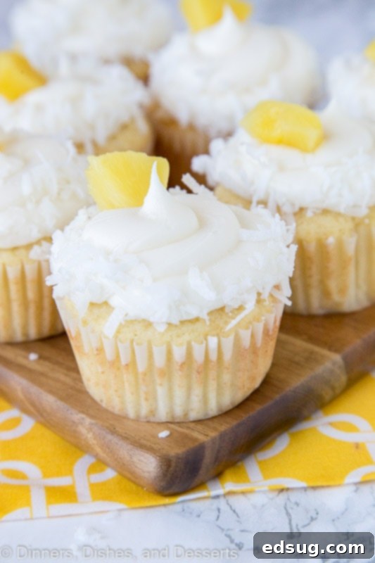 Tropical Pineapple Coconut Cupcakes 2 A close up of fluffy Pineapple Coconut Cupcakes with shredded coconut and a pineapple piece on top