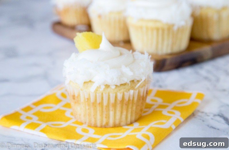 Tropical Pineapple Coconut Cupcakes 3 Two pineapple cupcakes with coconut and pineapple pieces arranged on a white plate