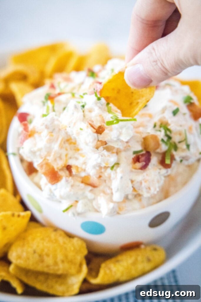 A chip expertly scooping a generous portion of creamy Cheddar Bacon Ranch Dip from a rustic bowl, showcasing the rich texture and visible pieces of bacon and cheddar.