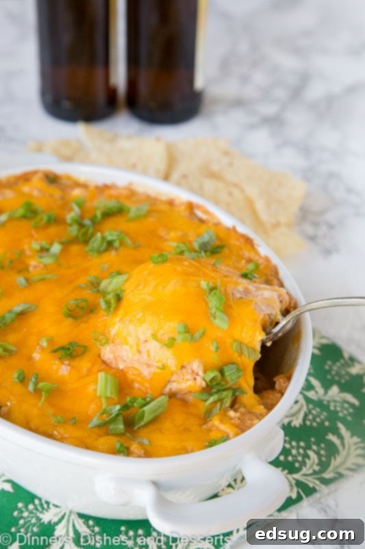 A spoon taking a scoop of creamy barbecue chicken dip from a baking dish, highlighting its cheesy texture.
